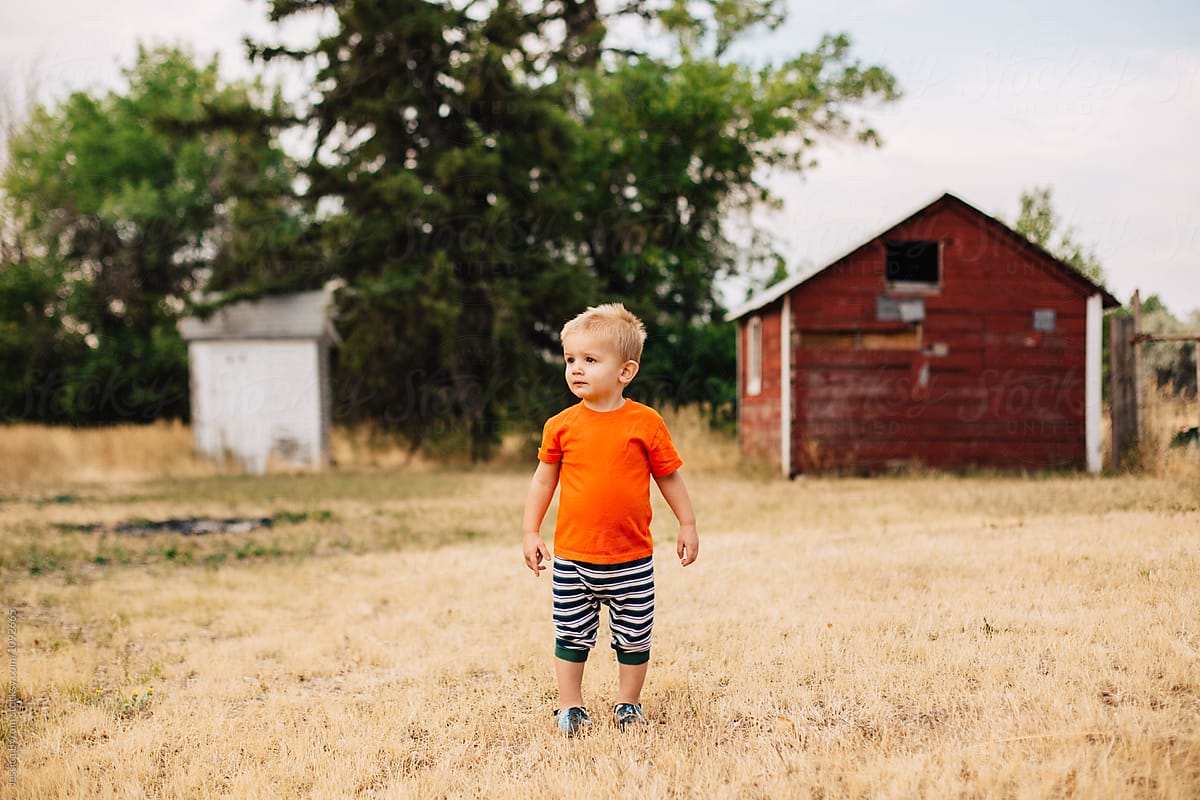 Cute toddler boy standing outside on a farm in the morning.