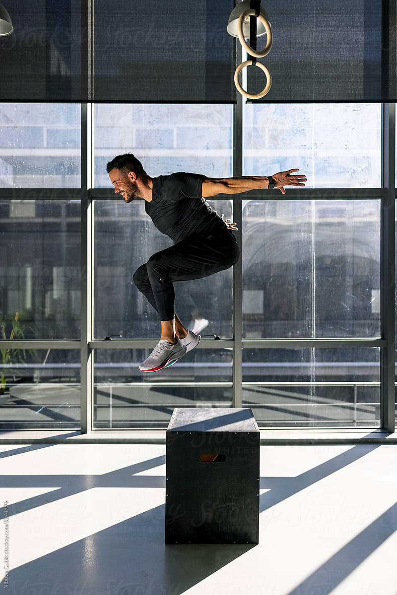 Side view strong man jumping above fit box during functional workout