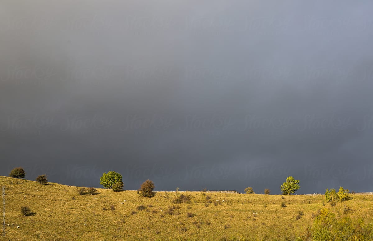 Stormy grey sky against a sunlit hilltop
