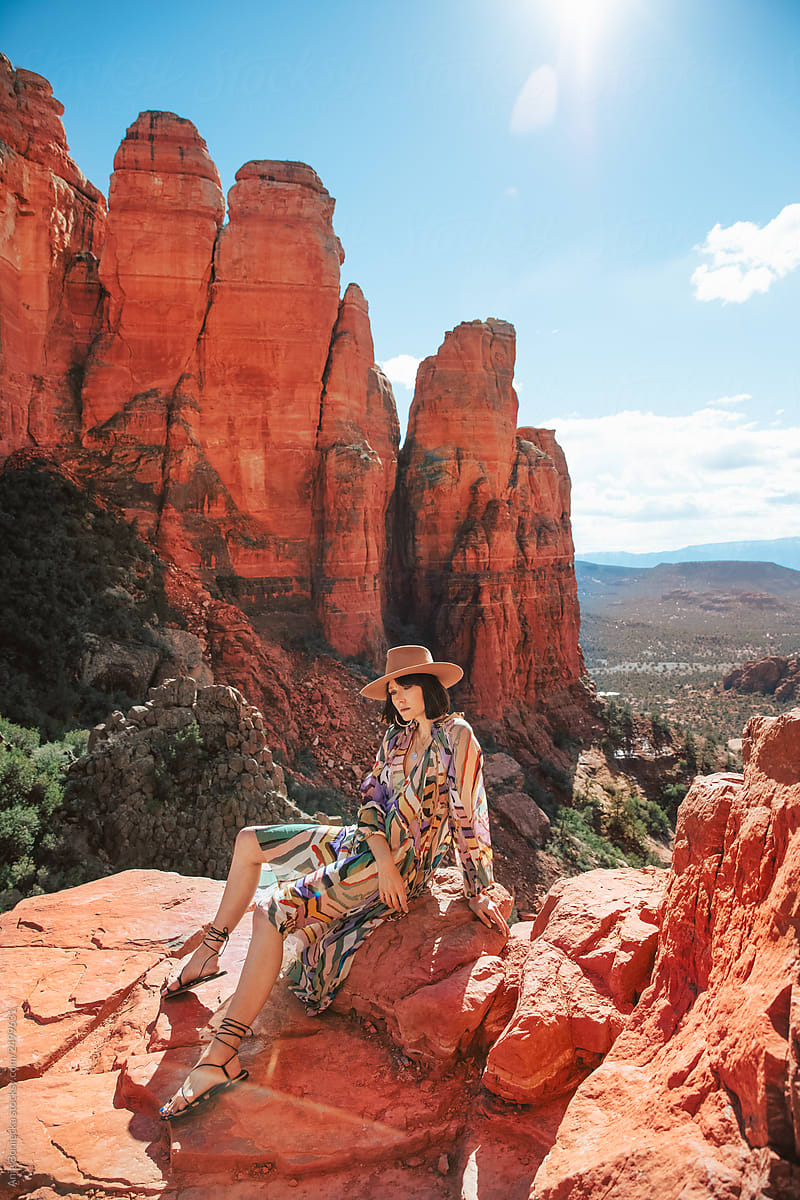 Stylish Cowgirl in dress sits on desert cliff.