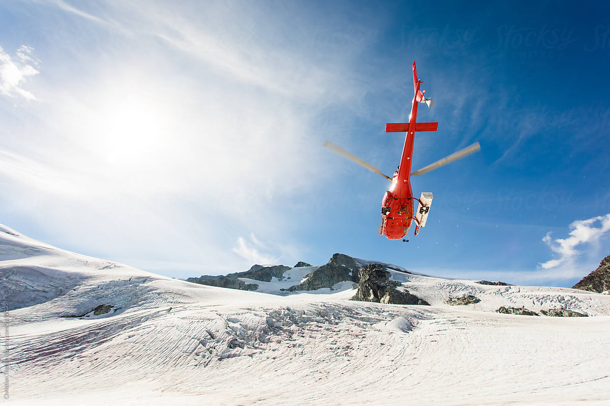 A helicopter flying on a sunny day in glacier covered mountains