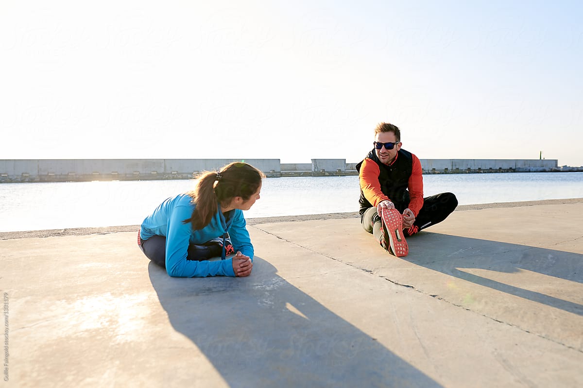 Couple of athletes stretching on pier.