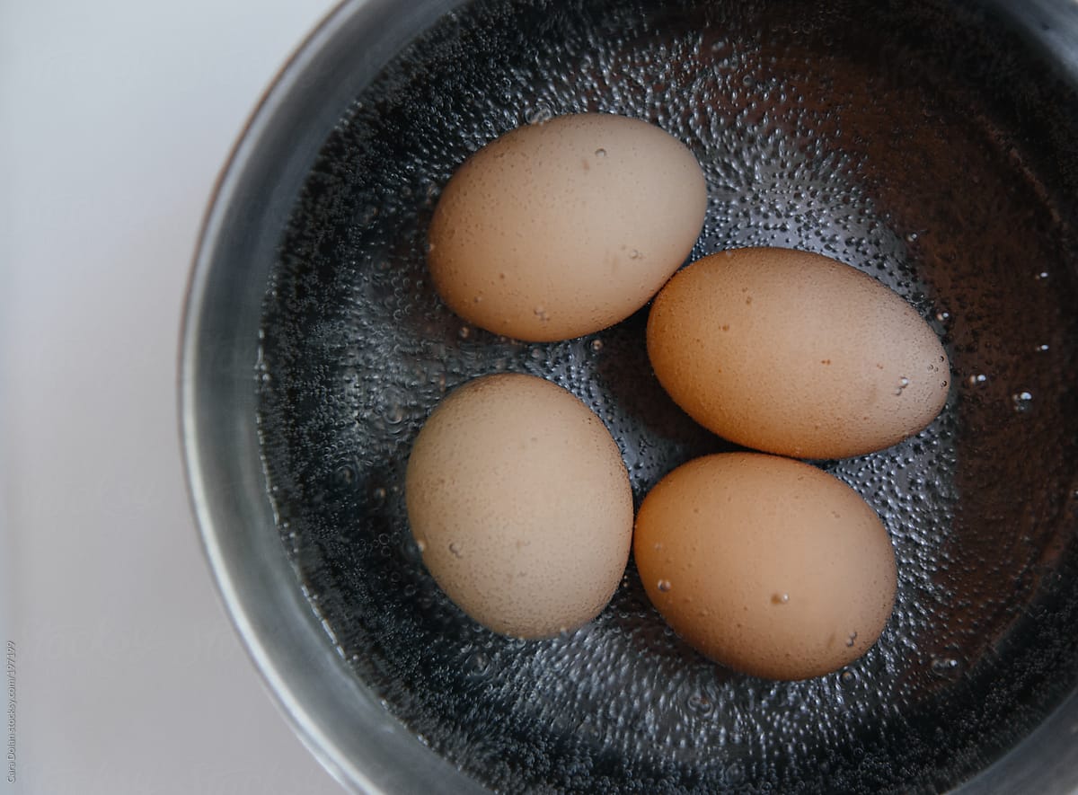 Four eggs boil in a pot of water on the stove