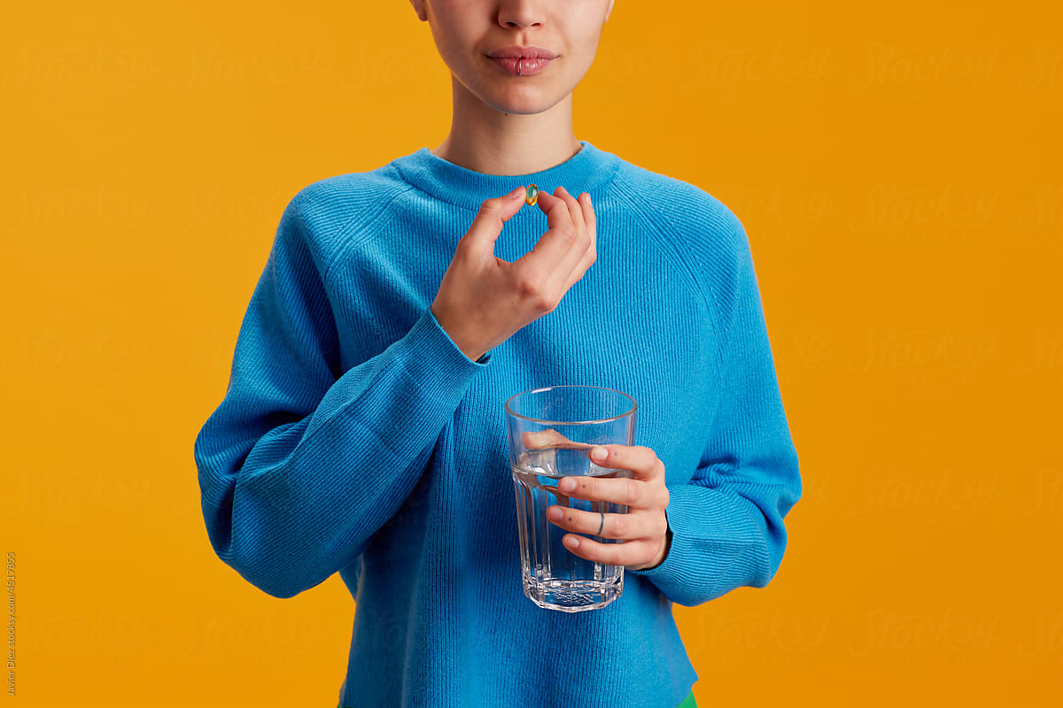 Crop teenager taking pill with water