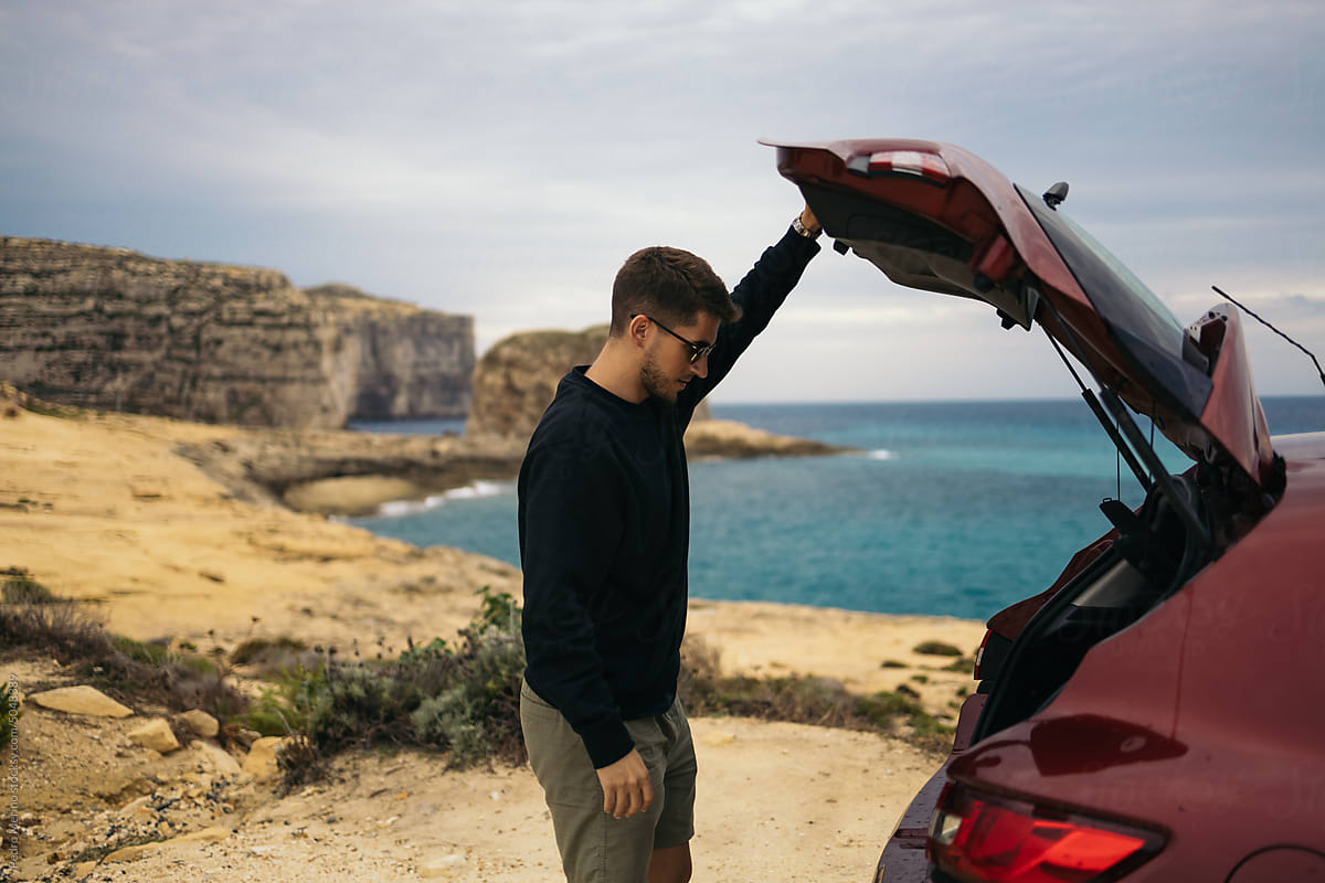 Young man opening the trunk of the car near some cliffs