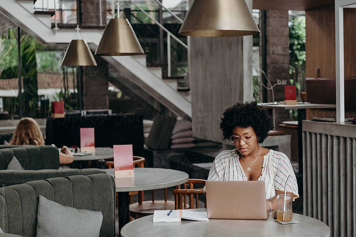 Stylish black woman working remotely in modern bar during day