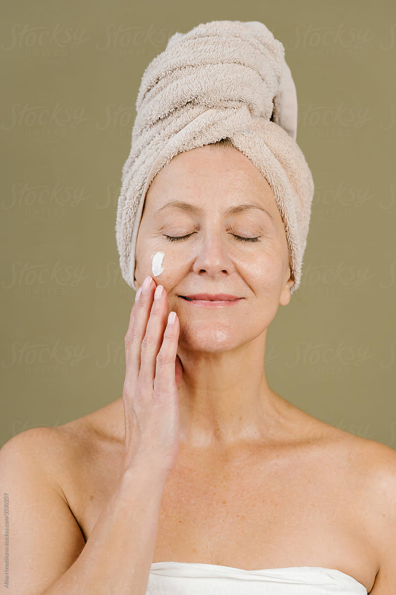 Dreamy woman applying facial cream in studio