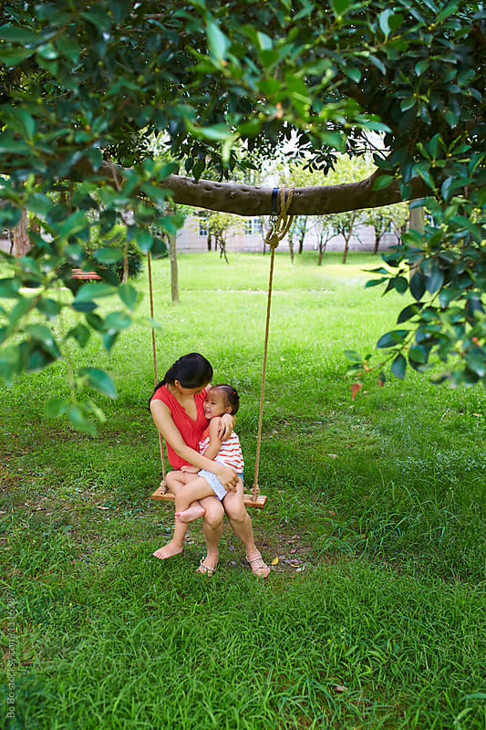 mother holding her little girl sitting on the swing under the tree
