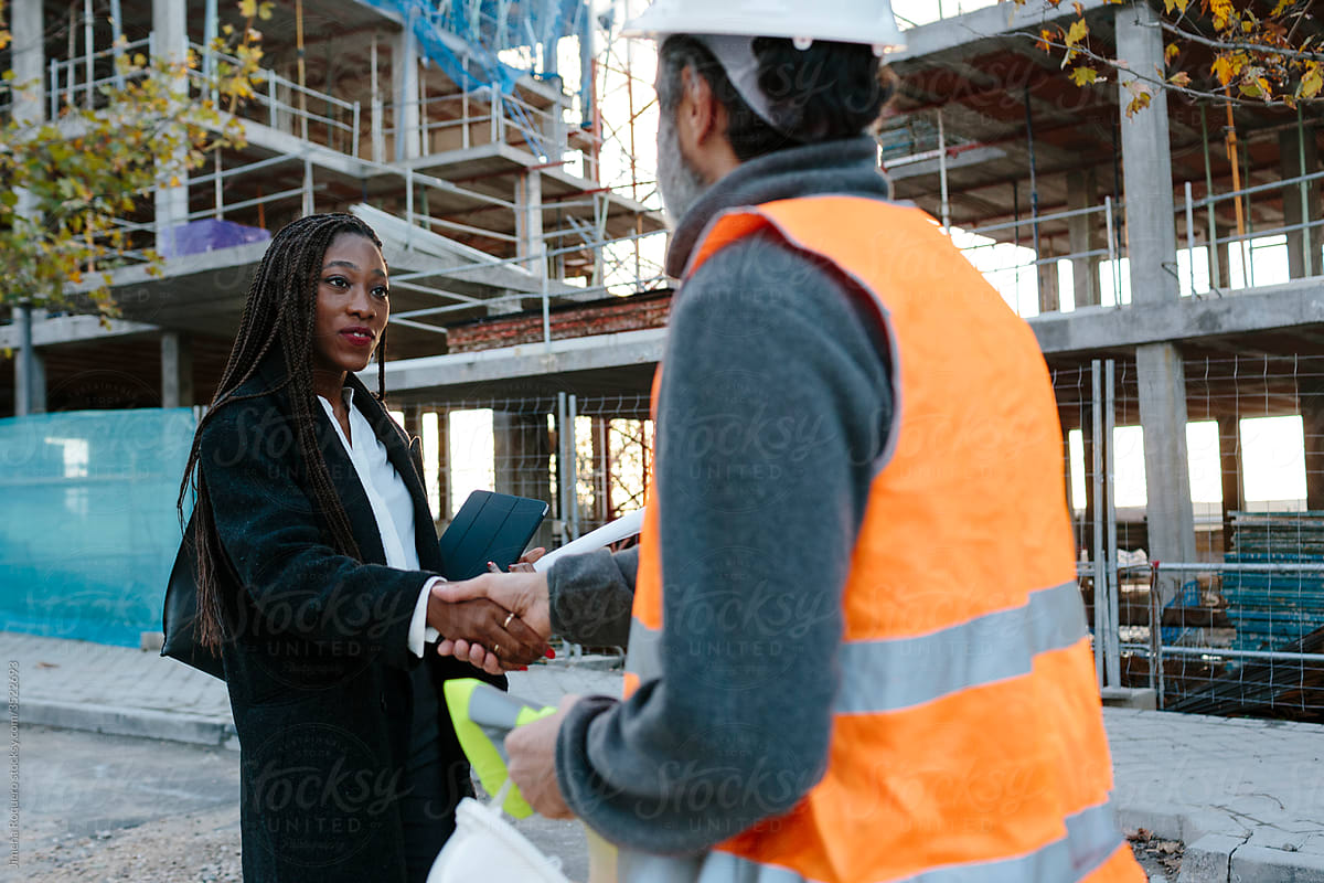 Woman engineer shaking hand with construction foreman in front of construction.
