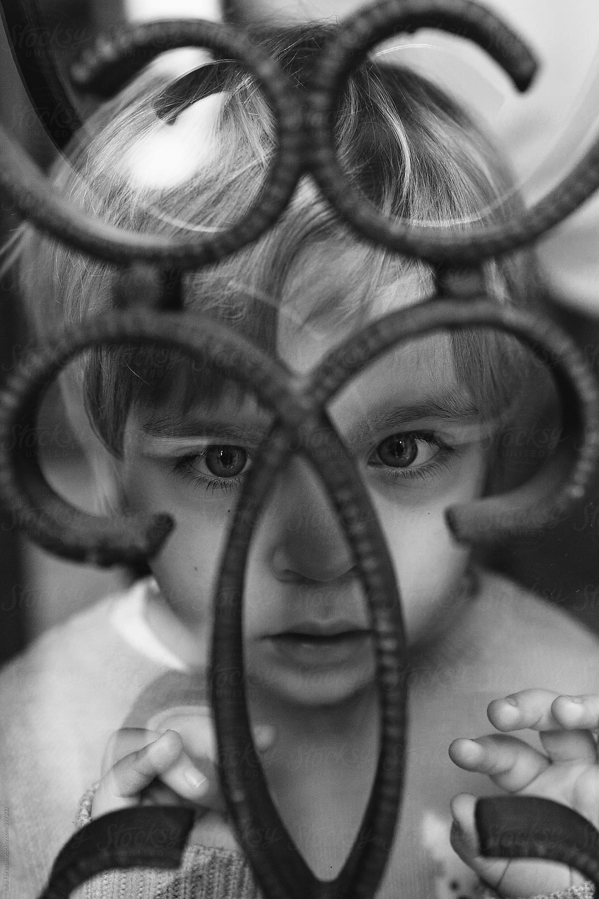 Little girl stares intensely through the curved metal bars on a window.