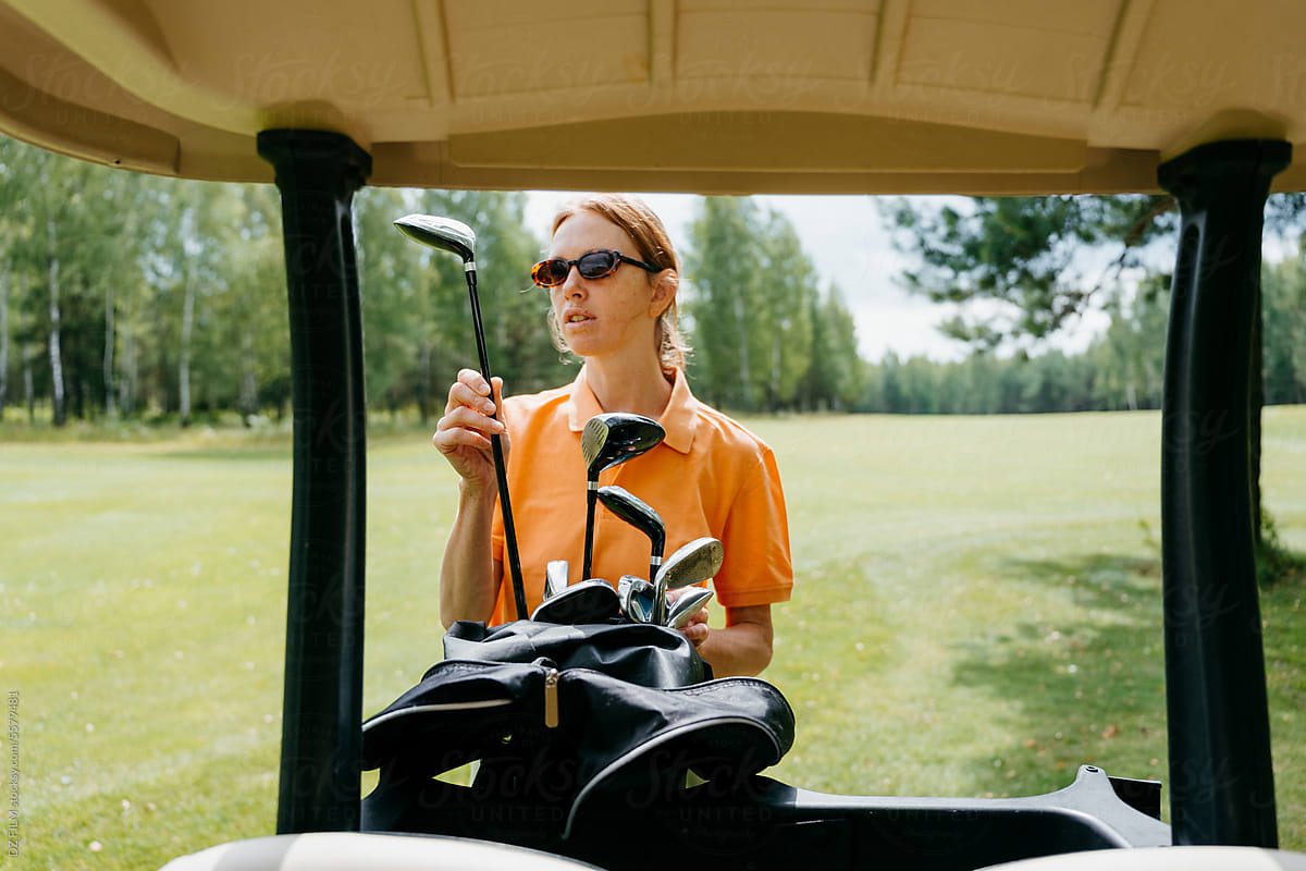 A woman with a golf club stands on a golf court
