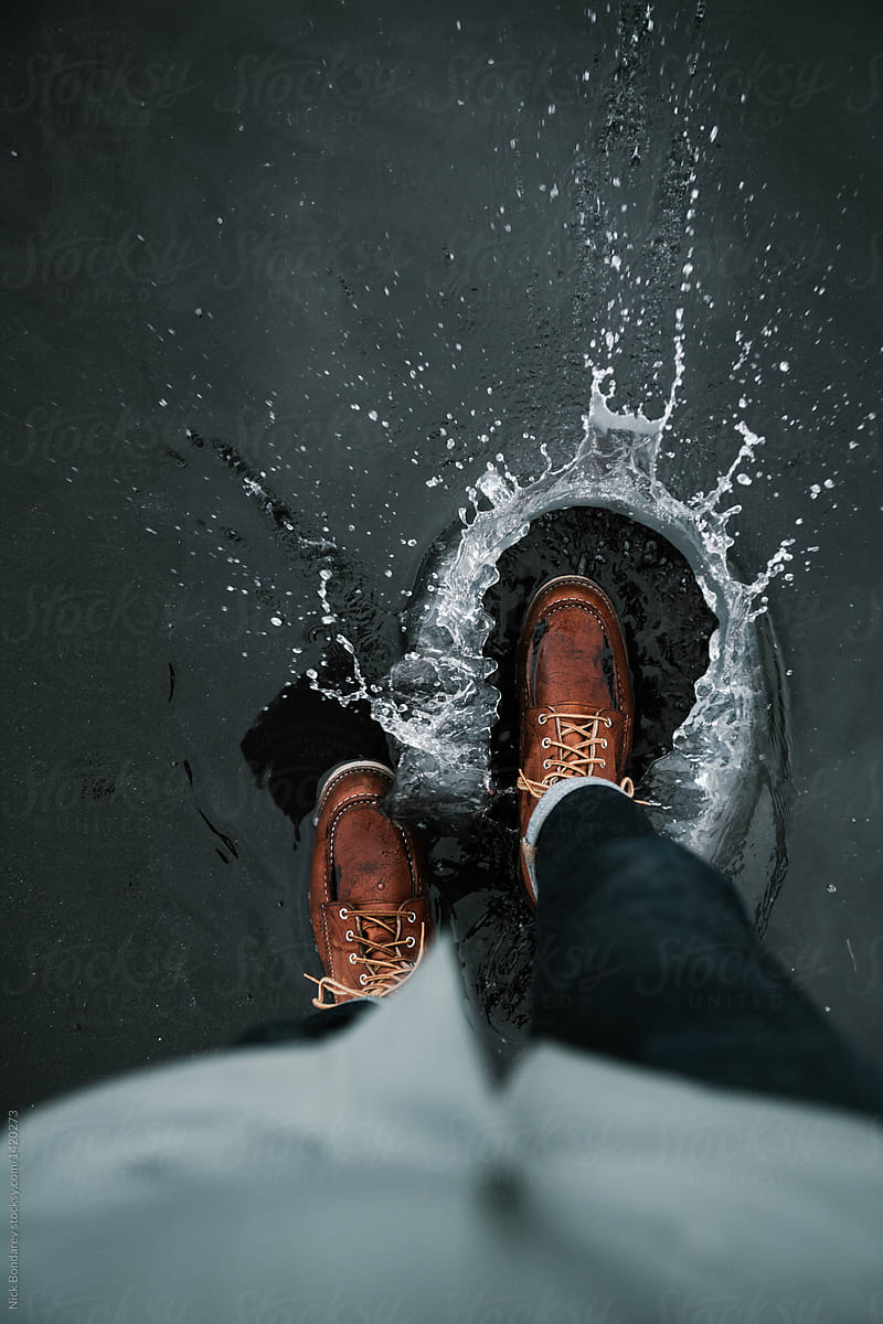 Anonymous man walking in waterproof leather boots  in puddle outdoors, from above Human in boots and jeans on puddle