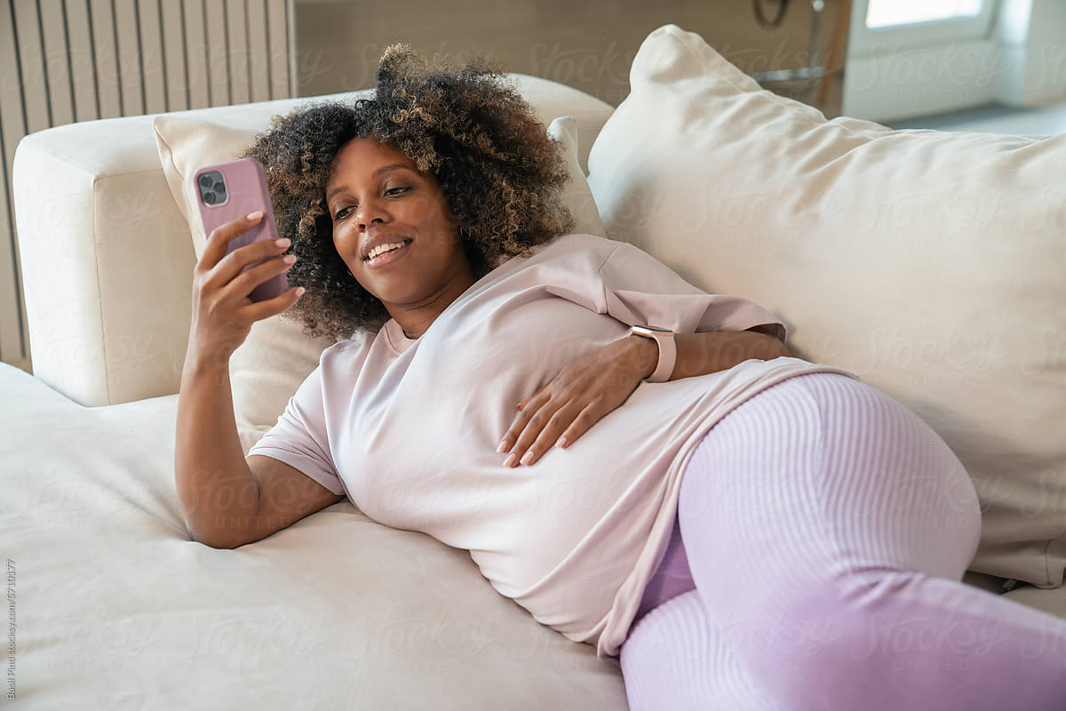 Pregnant woman lay on couch at home and browsing smartphone