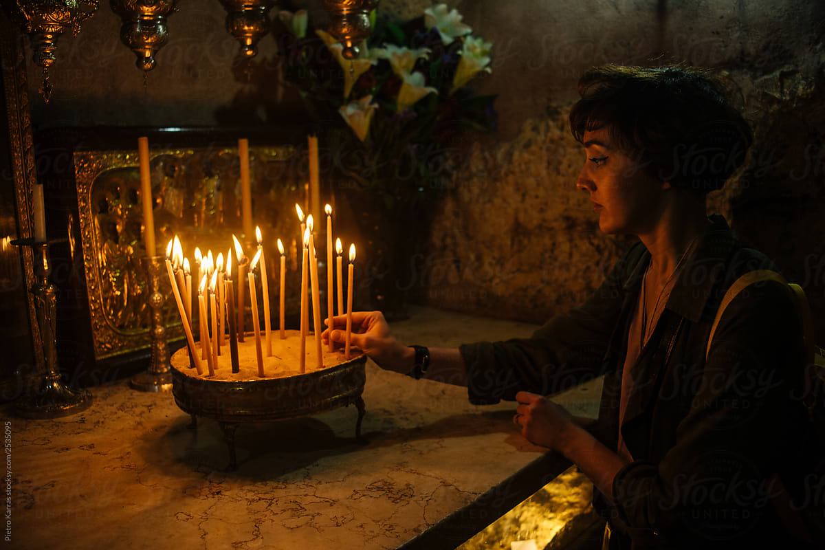 Young woman putting candle in bowl in church