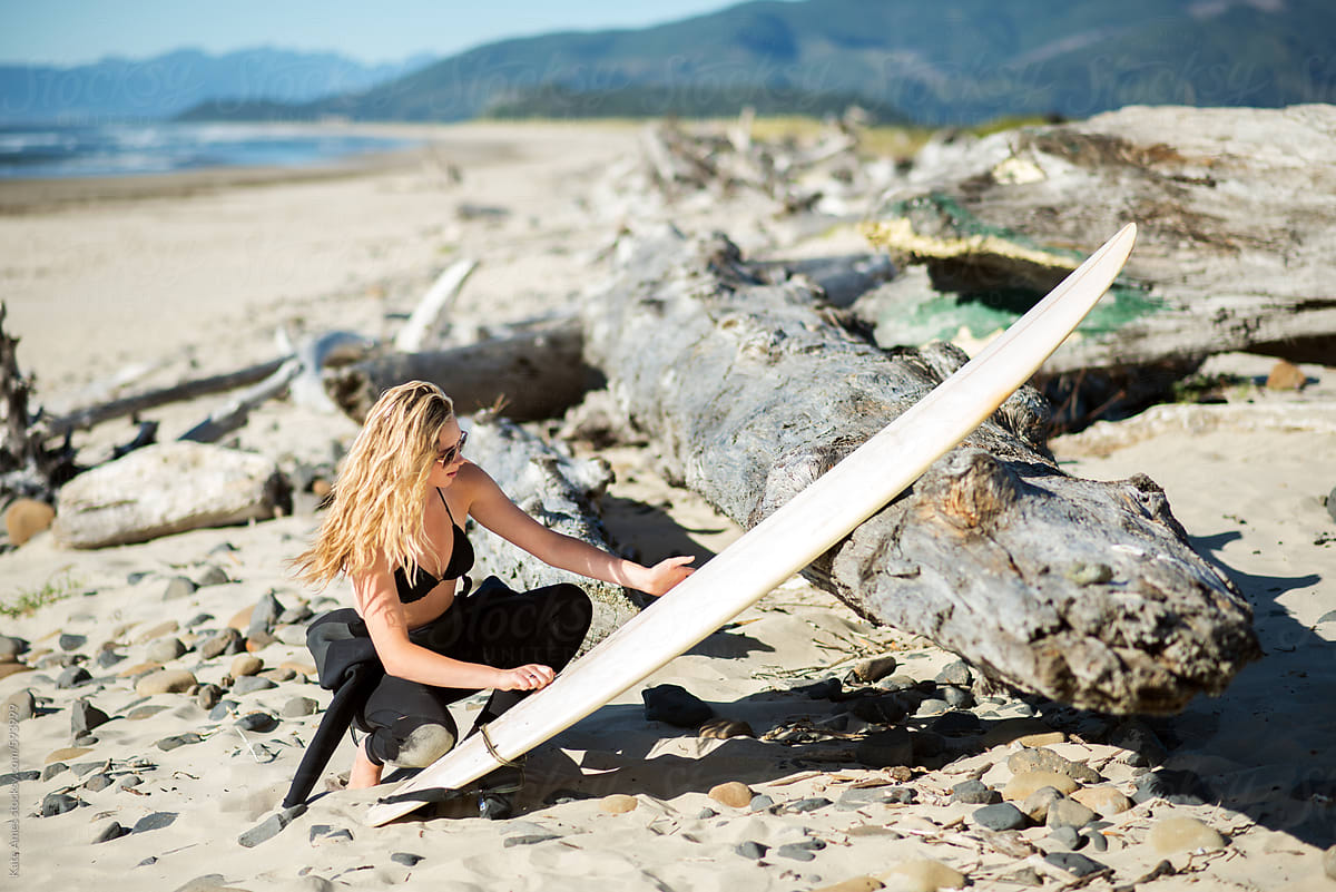 Young beautiful blonde surfer chick waxes her surfboard.