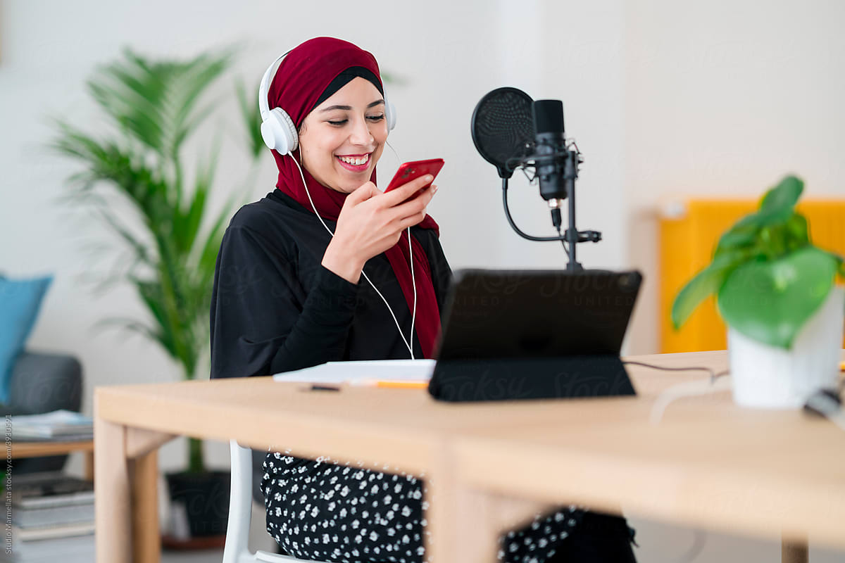 Cheerful Arab woman recording voice message on smartphone