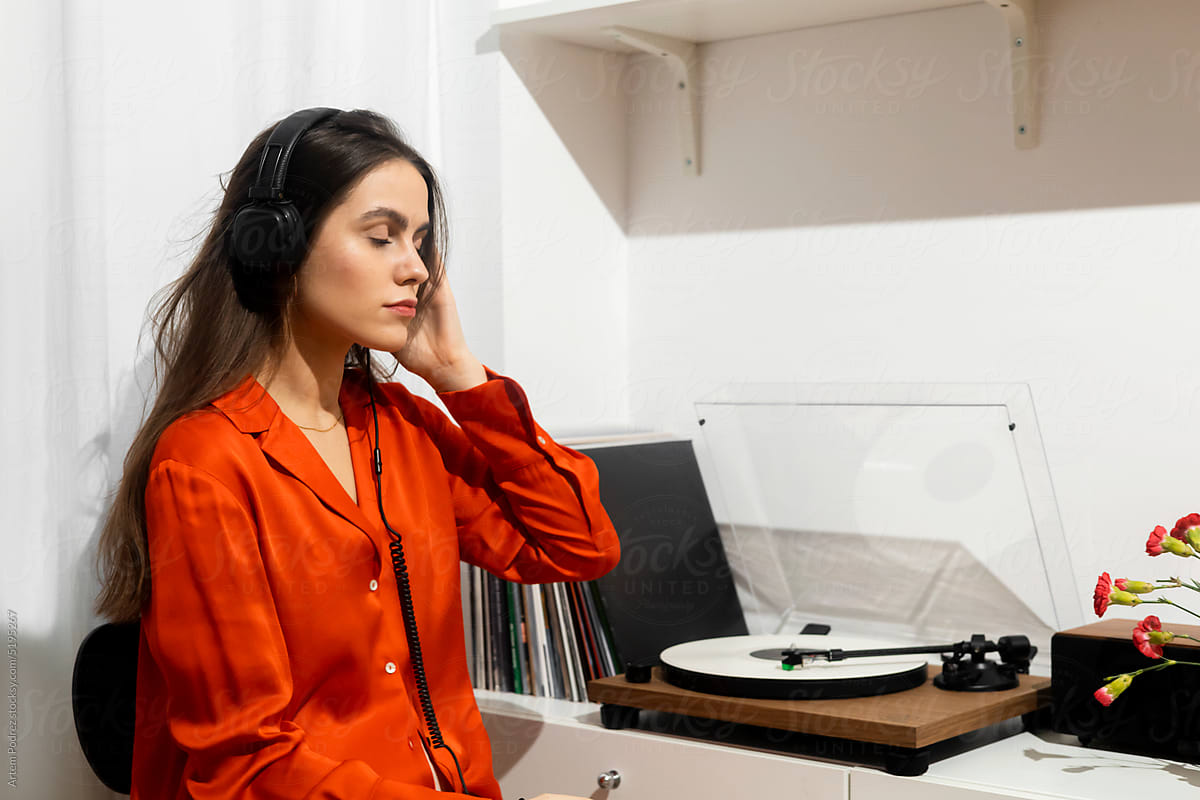 Woman in a red shirt listens to music on a turntable with vinyl record