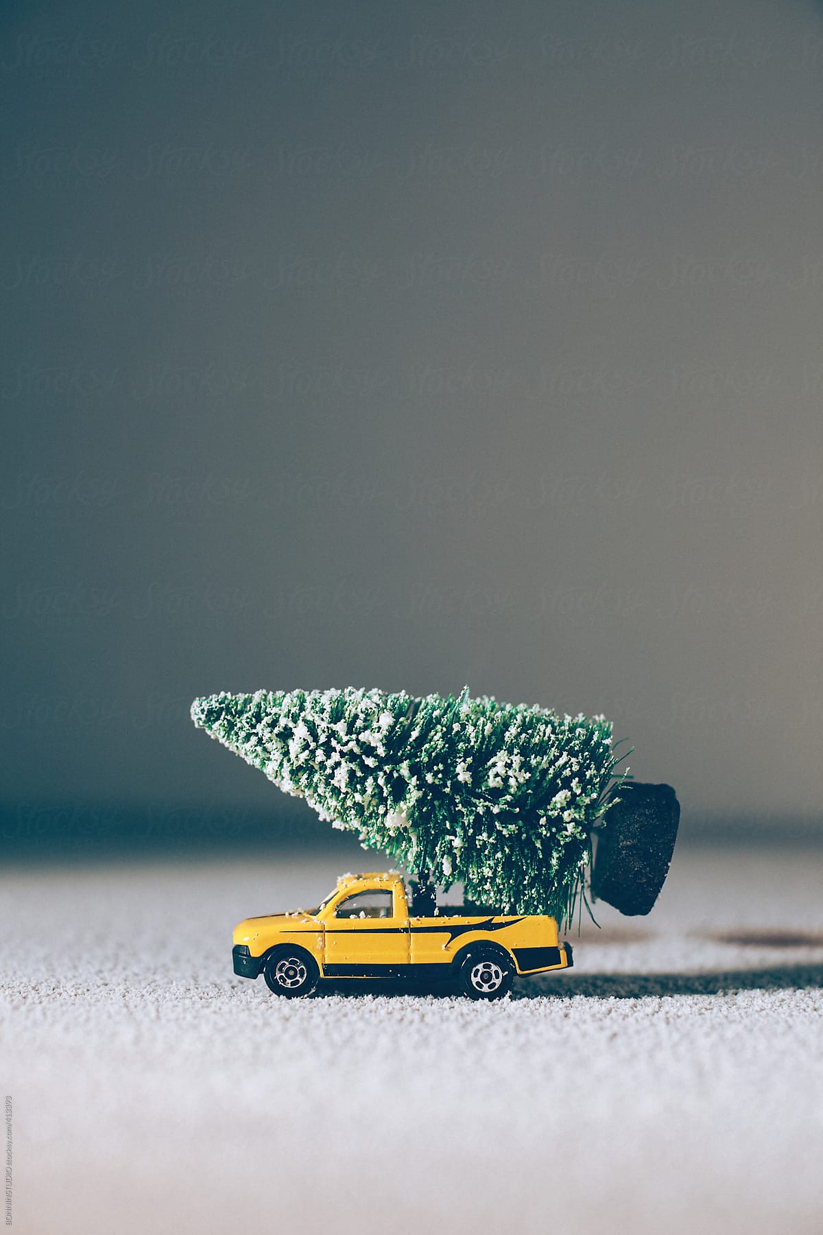 Christmas tree on yellow toy car over grey background.