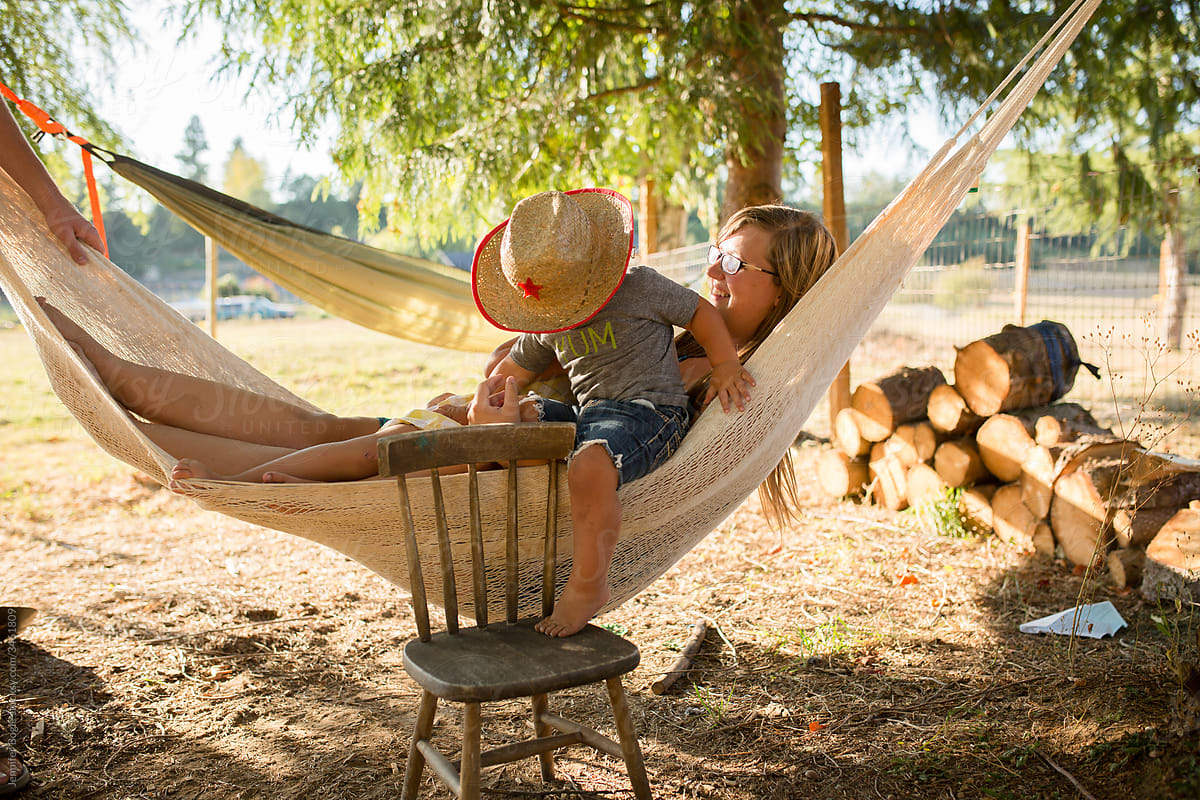 Toddler in straw hat  climbs into hammock with his mother