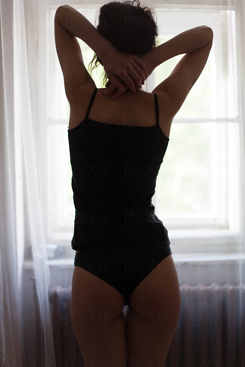 Woman in a black underwear standing near the window. From the back.