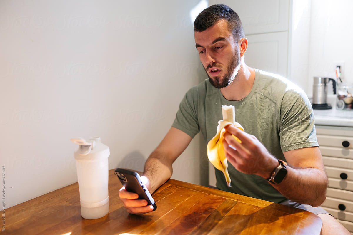 Man looking at phone while eating banana before a workout.