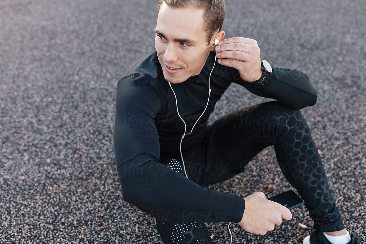 Positive male athlete putting on earphones