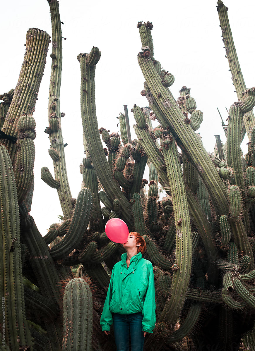 Standing woman blowing up a balloon with big dangerous cactus