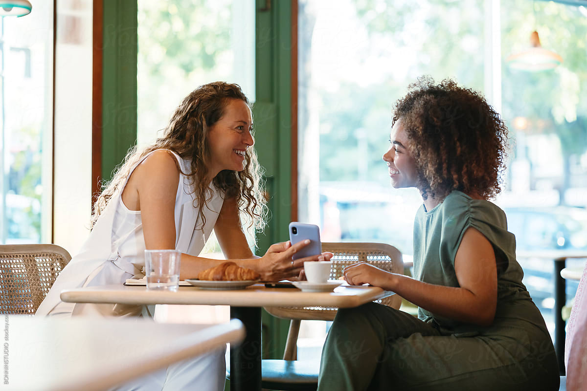 Multiracial girlfriends with cellphone chatting in cafe