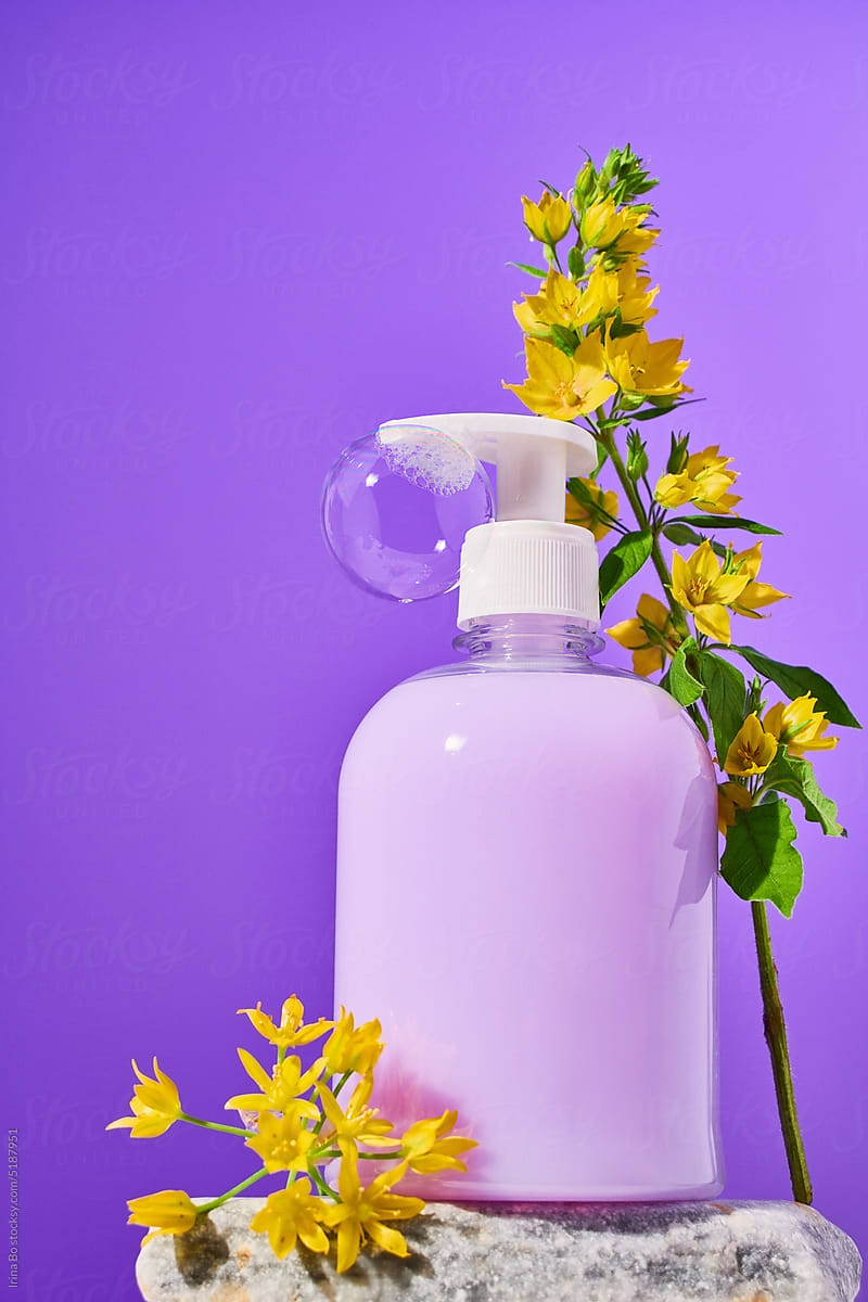 Bottle of liquid purple soap with a soap bubble stands in flowers
