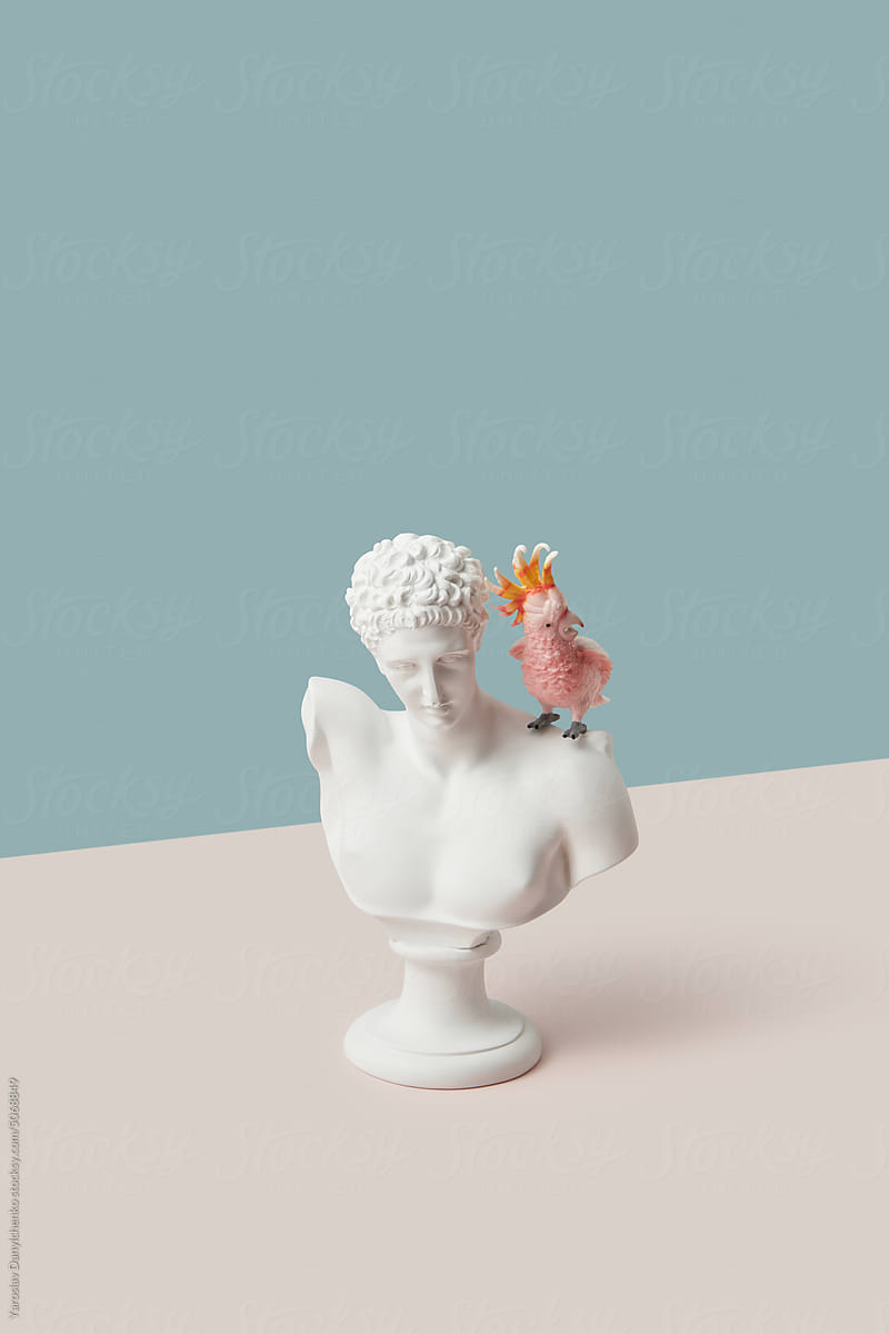 Antique bust with pink toy parrot on shoulder.