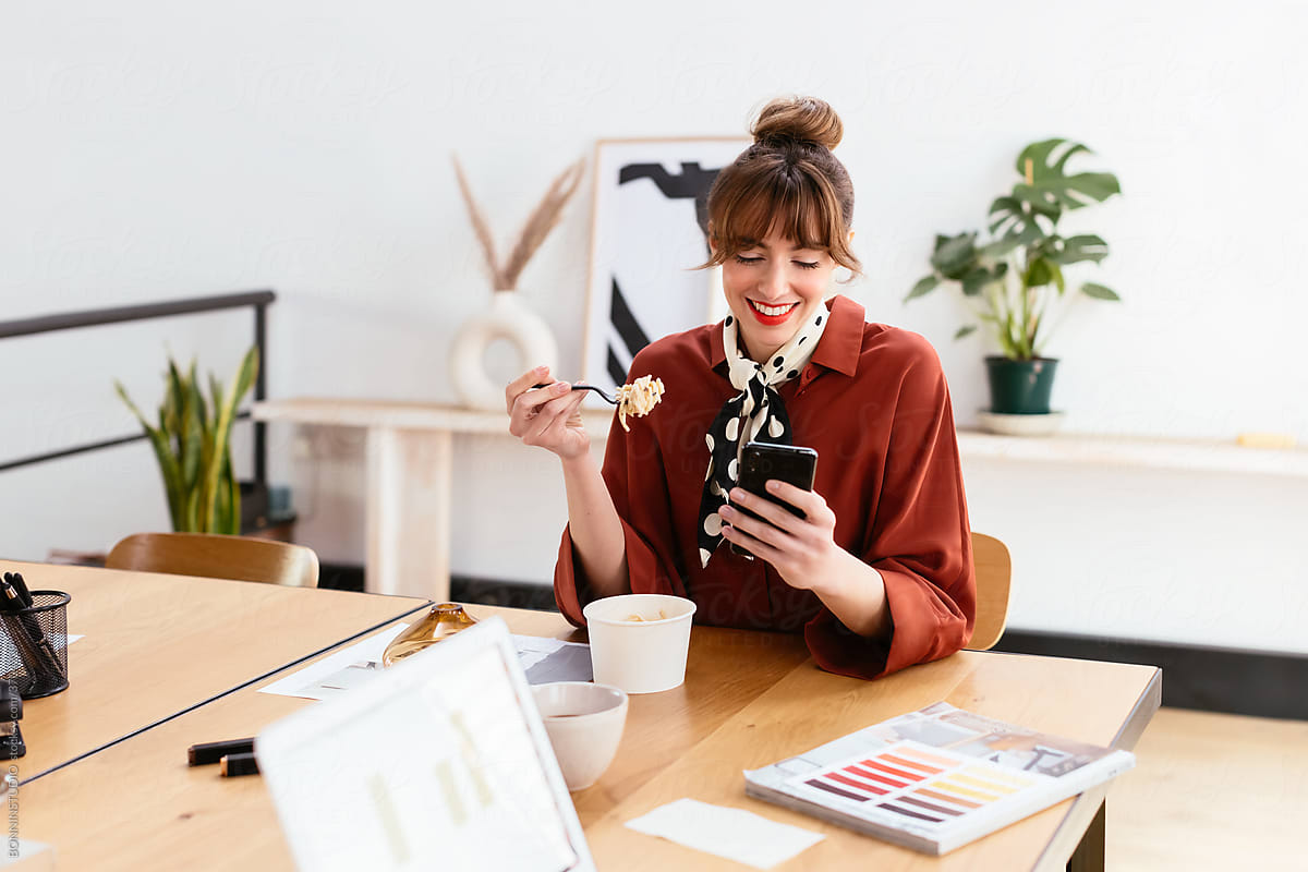 Cheerful female designer using smartphone during lunch