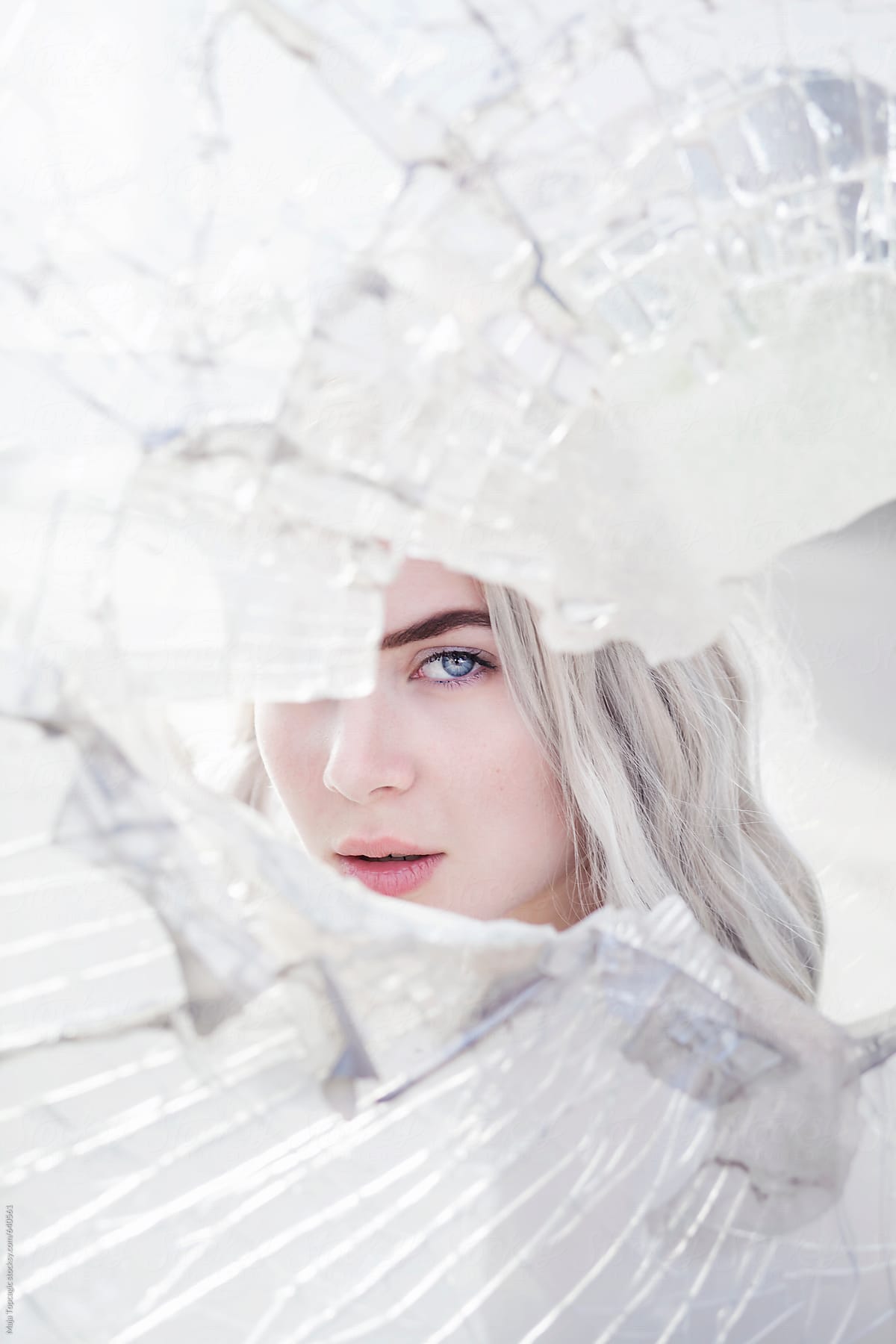 Young beautiful woman with grey hair and blue eyes looking through broken glass