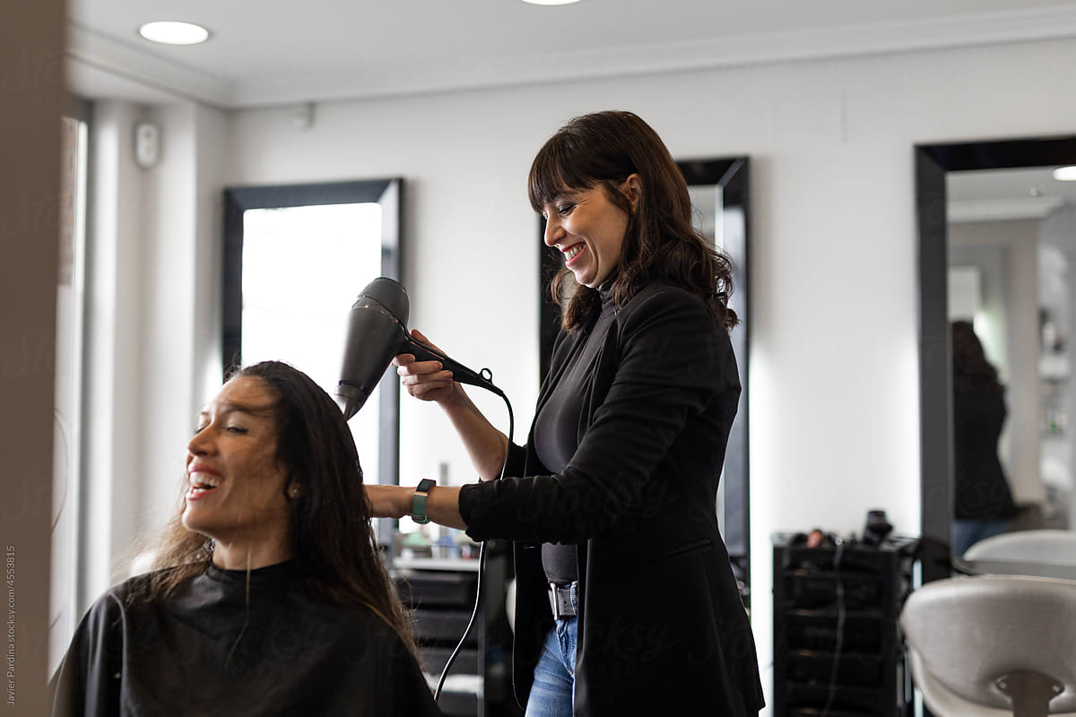 Shot of a cheerful hairdresser blow drying hair of a woman
