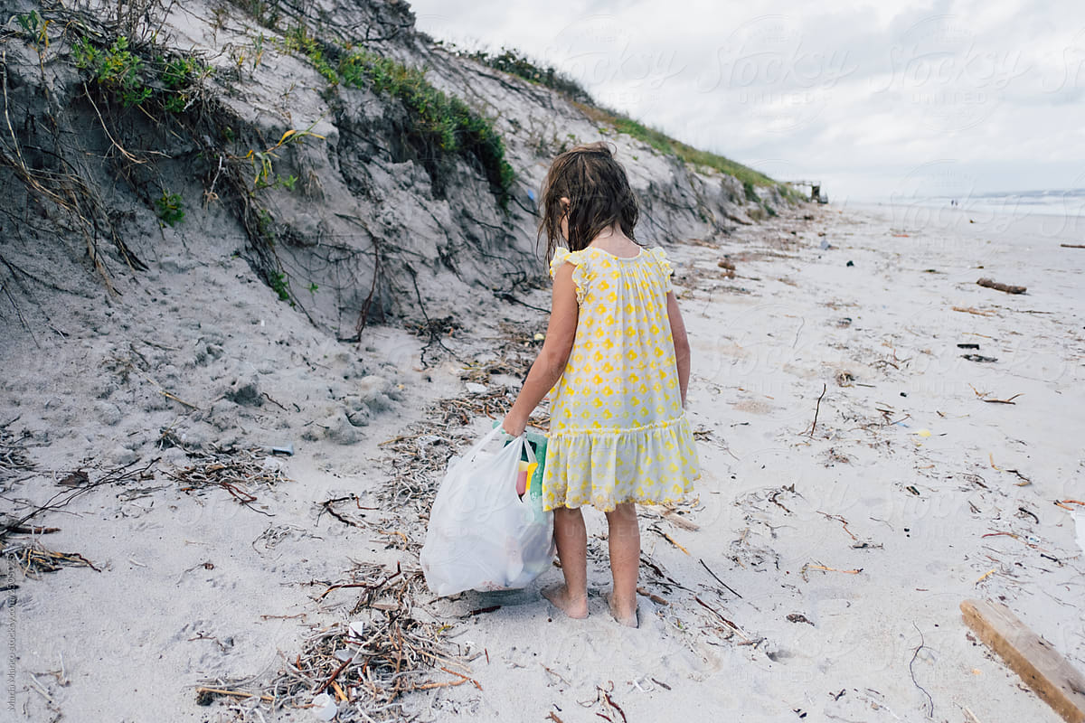 young child picks up plastic trash from beach