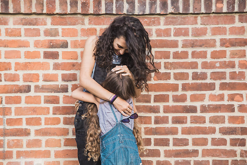 Mother and daughter embracing in front of a brick red wall