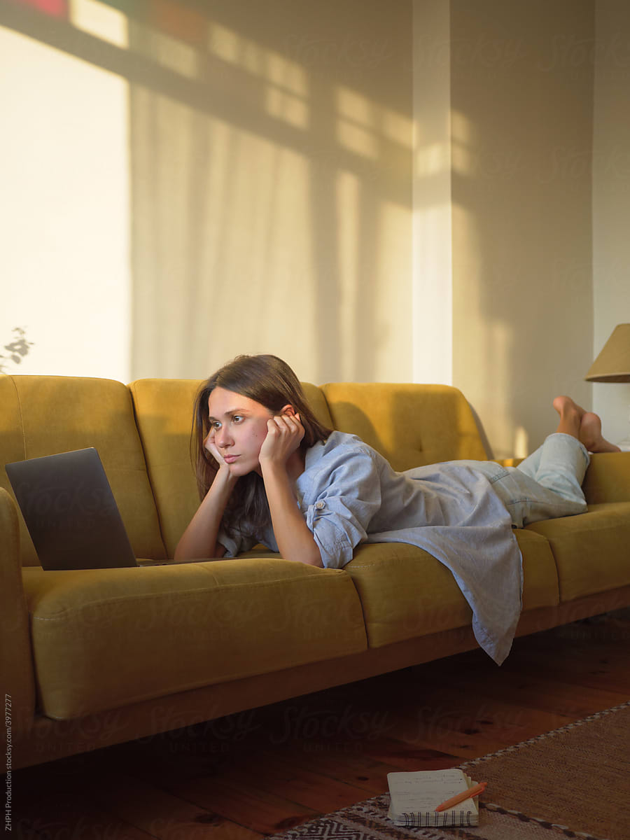 Woman with laptop and notebook laying on the sofa at home