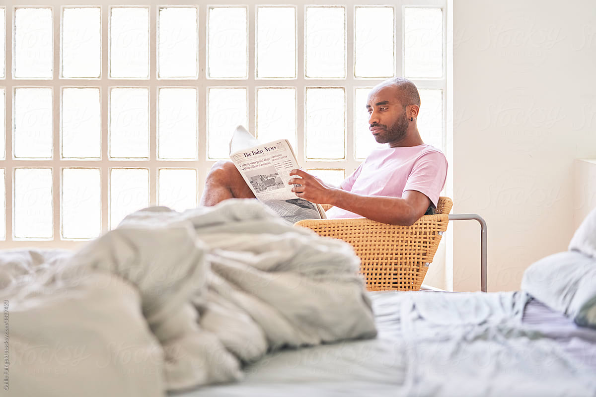 Black man sitting in chair and reading newspaper.