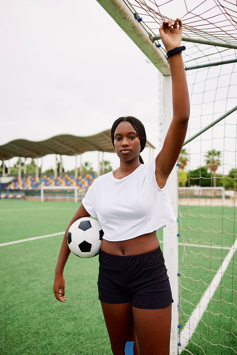 Teen black girl with ball standing near goal on field