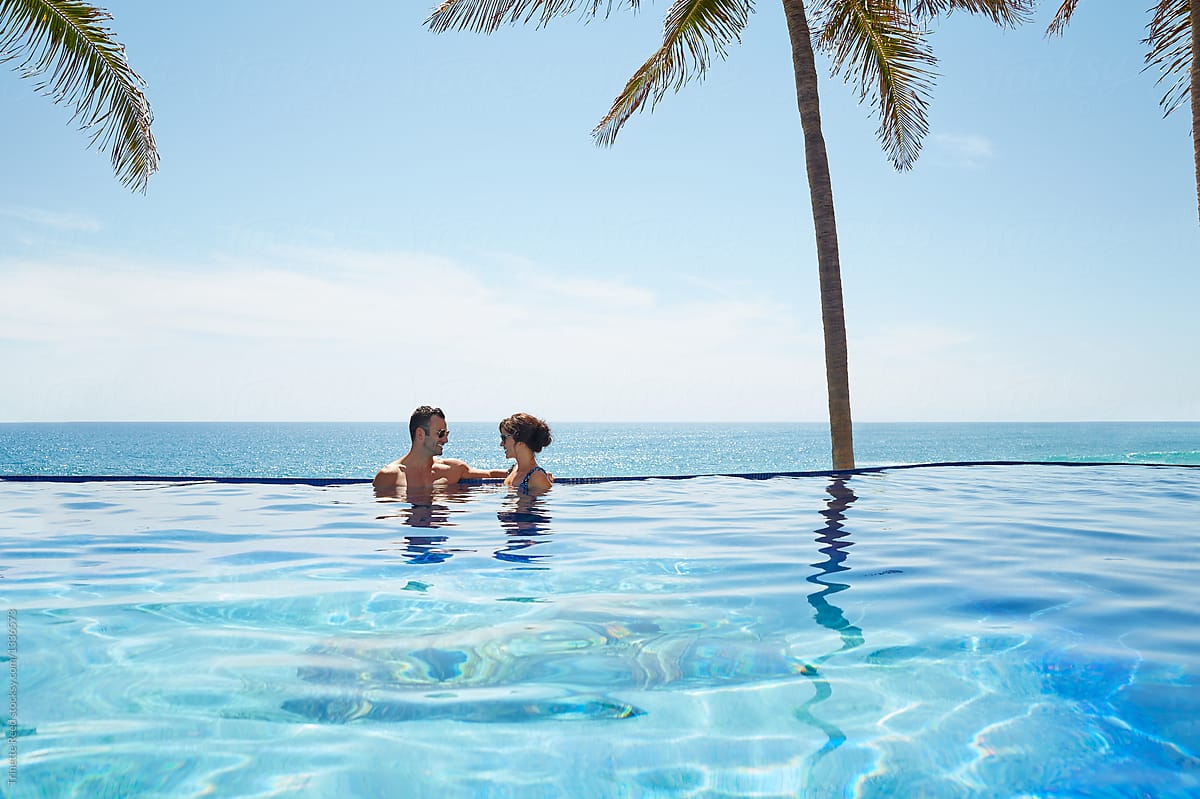 Couple relaxing on edge of infinity pool overlooking ocean on vacation