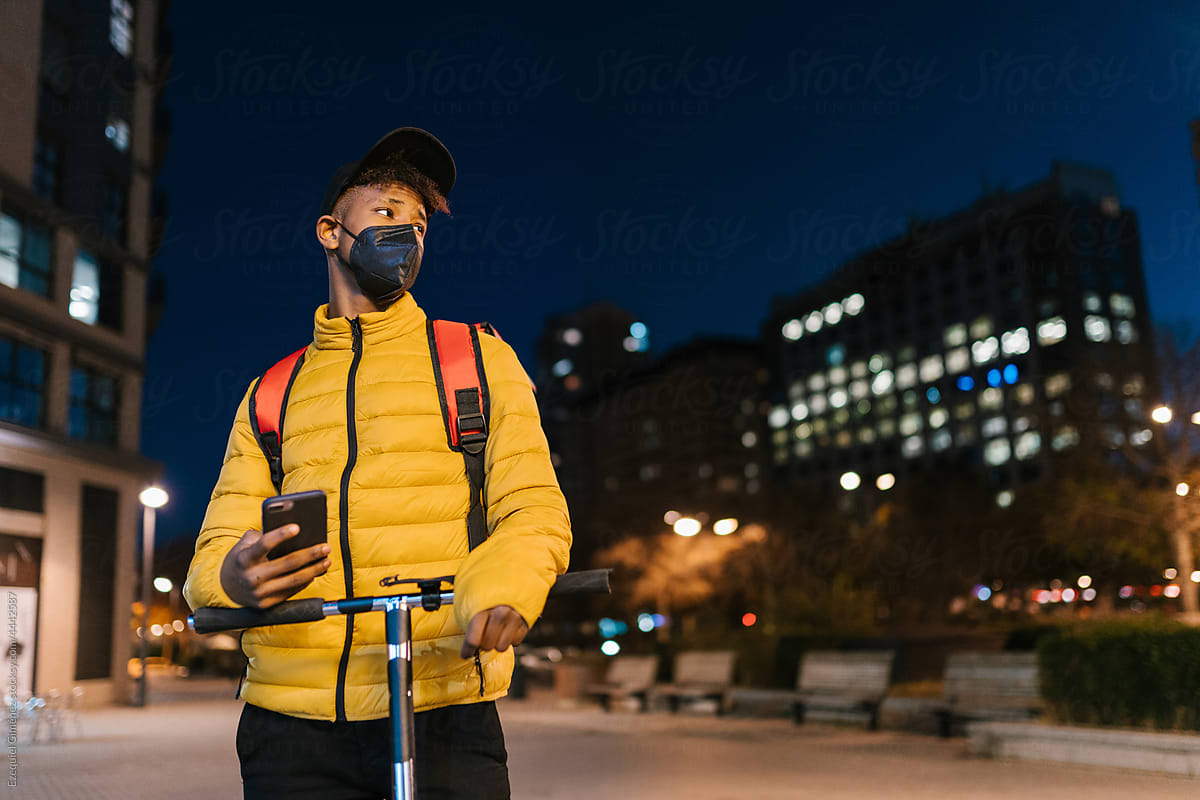 Serious black courier on scooter using smartphone