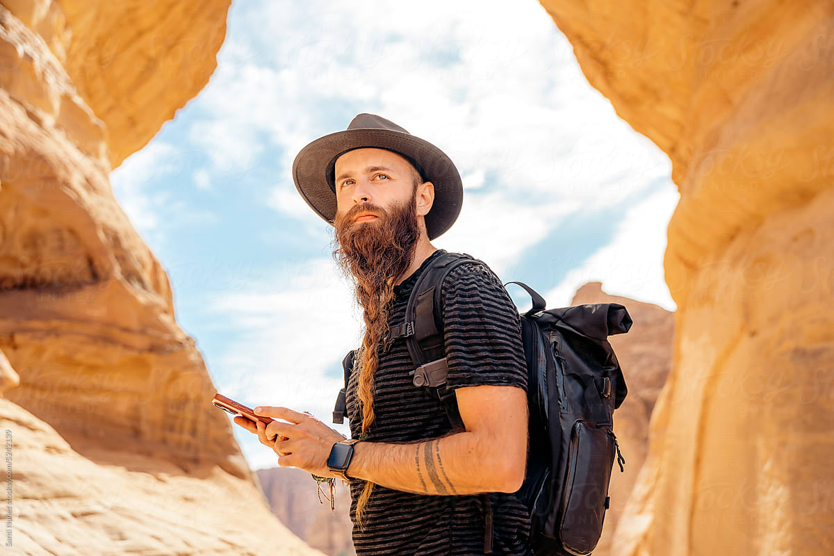 Traveler with beard and hat using a mobile in the desert