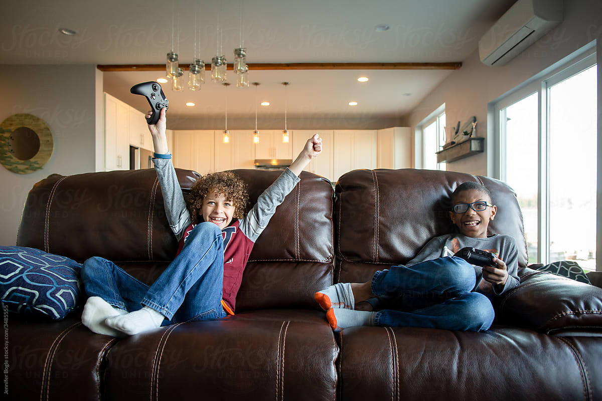 Boy playing video game with friend raises hands in victory