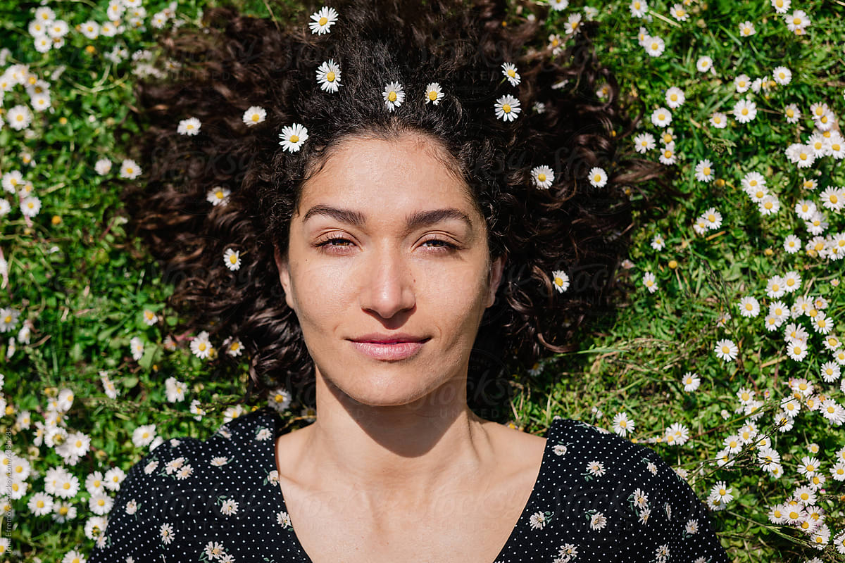 Woman covered with daisies laying on the grass looks up