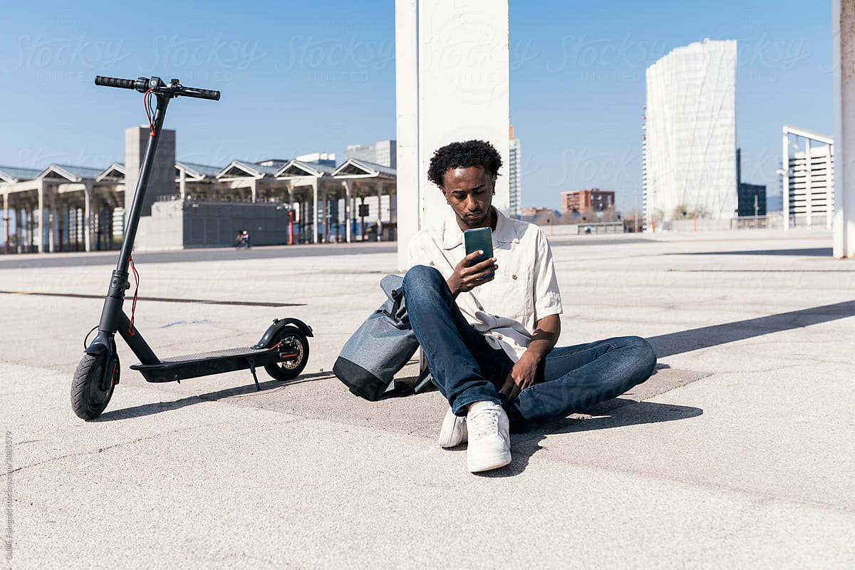 Stylish black man with scooter and phone in city