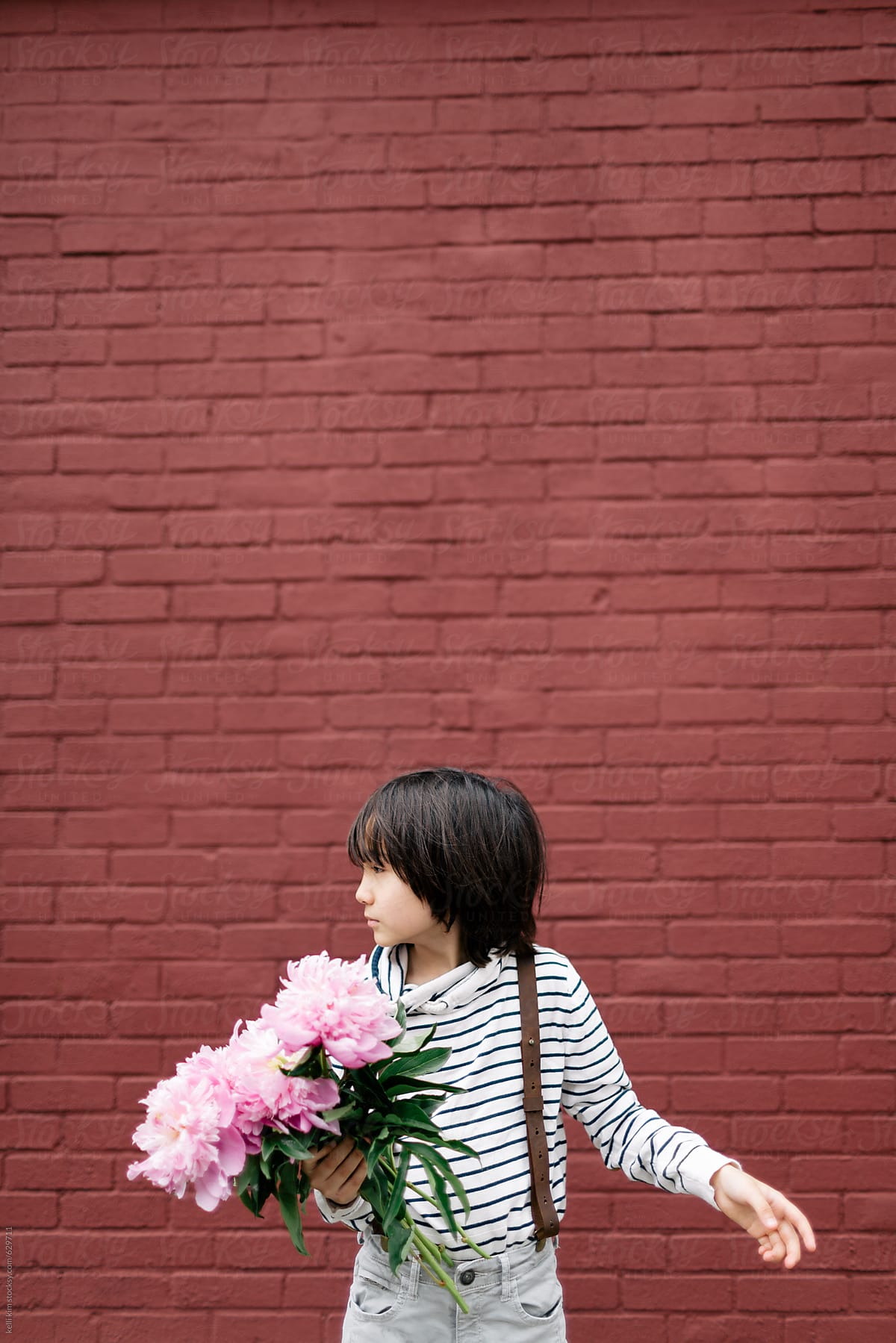 Cute mixed race boy holds pink flowers in front of brick wall