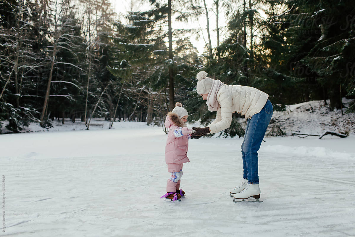 Mother holding hand of little kid while skating on ice