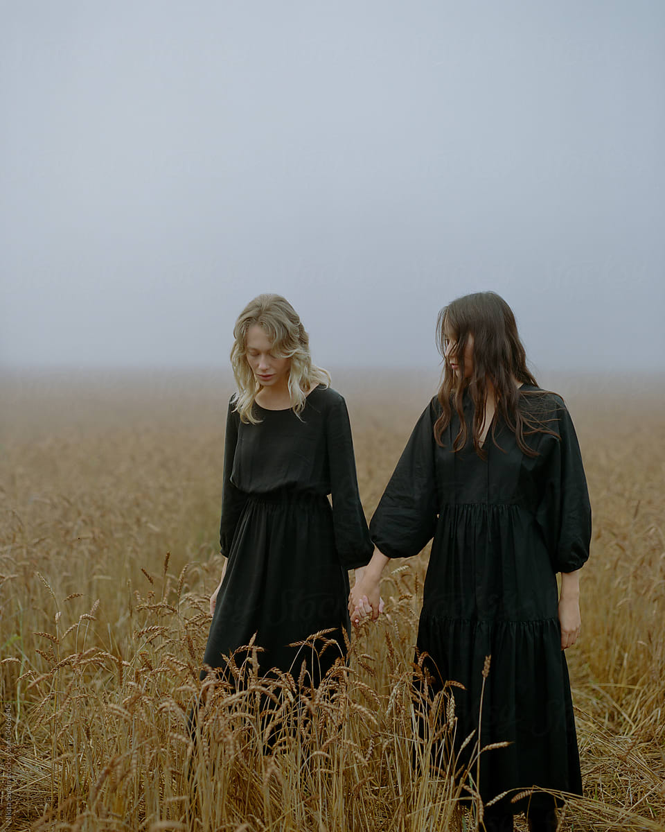 two beautiful girls in black dresses posing in a wheat field