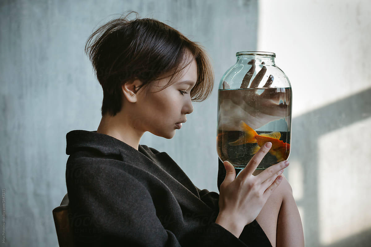 Asian Girl With An Aquarium Fish In A Dark Room. by Stocksy