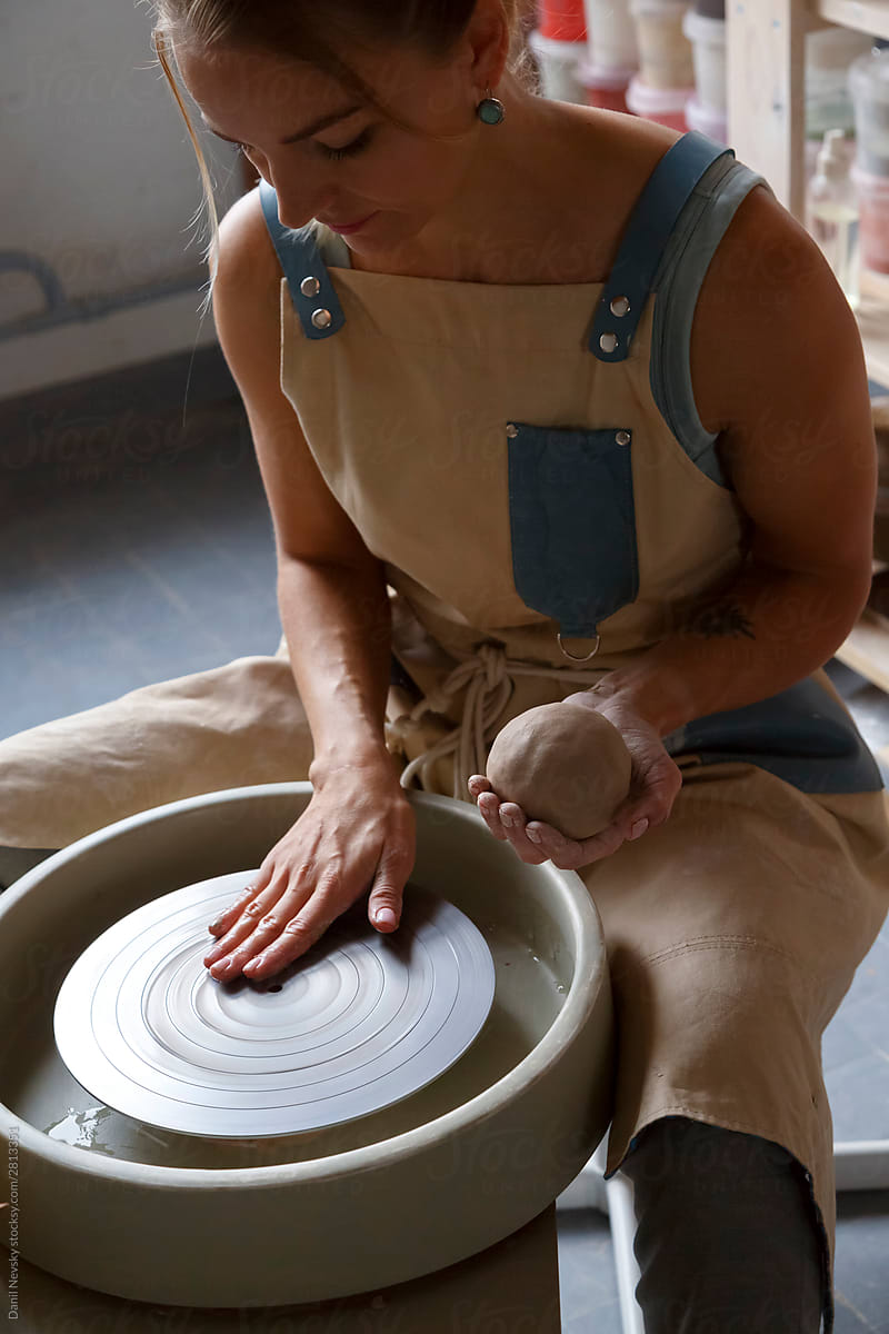 Female master in apron starting work with throwing wheel at workshop