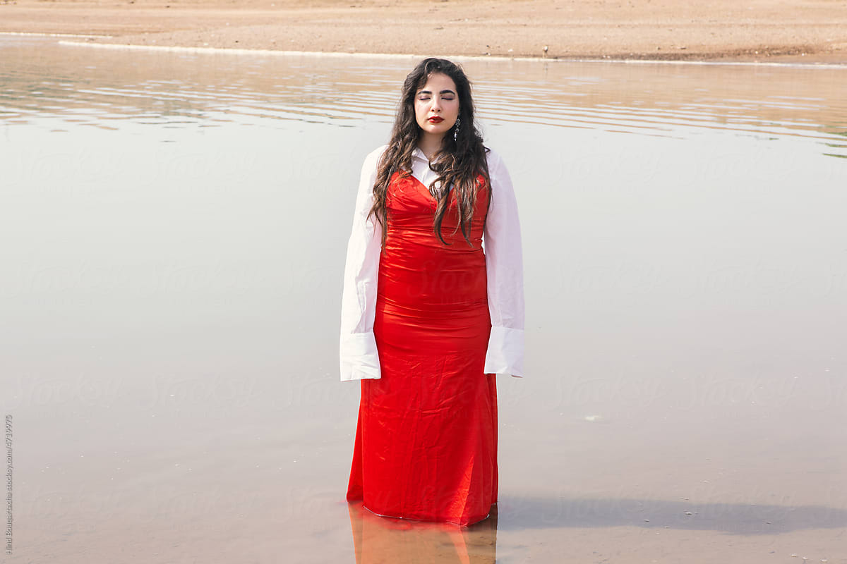 beautiful girl with long hair wearing red dress standing on the river